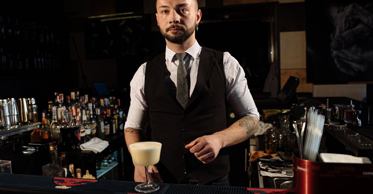 Professional bartender in a stylish lounge bar serving a creamy cocktail with confidence and charisma.